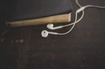 White ear buds and a Bible on wood
