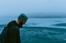 man with a thick beard walking on a lake shore in winter 