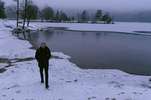 man walking on the snowy shore of a pond 