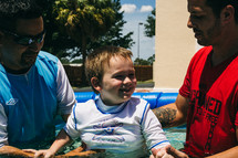 A young boy being baptized in a small swimming pool.