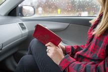 A woman sitting in the car passenger seat reading the Bible