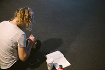 a girl writing in a journal with an open Bible on the floor 