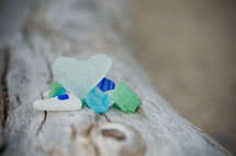 Blue, white and green colored stones,one a heart shape, laying on a tree trunk