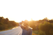 a woman in a hat standing on the side of the road 