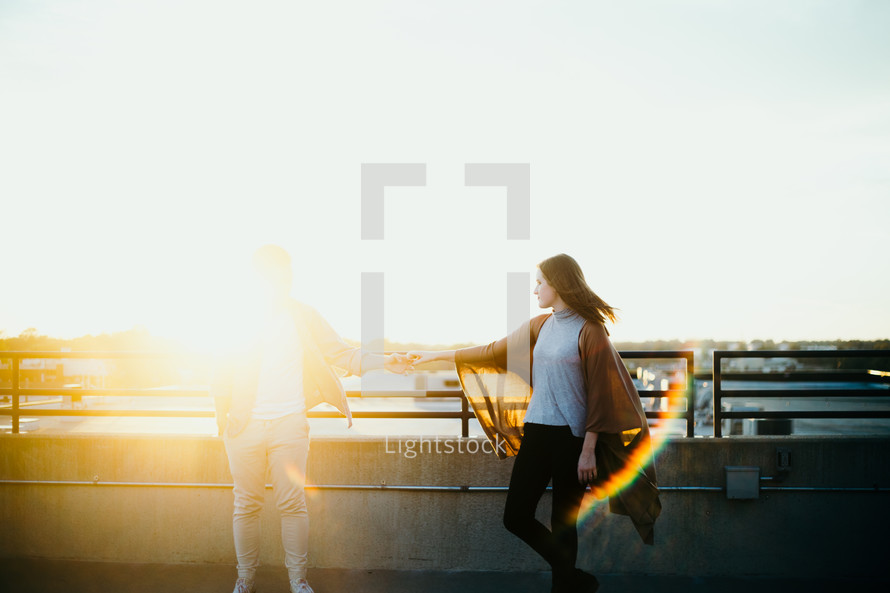 couple standing on an overpass holding hands in bright sunlight 