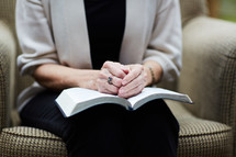 elderly woman with hands on a Bible in her lap 