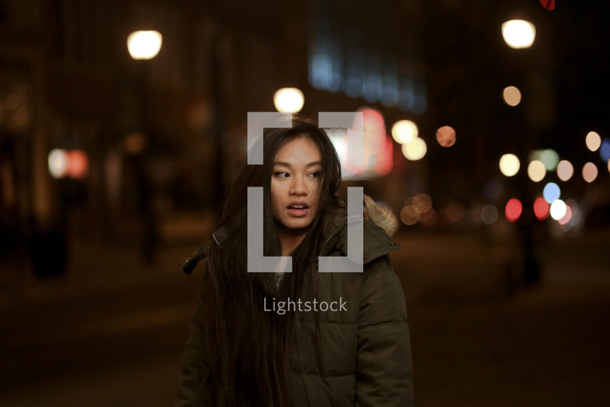 a young woman standing outdoors in a city at night in a coat 