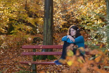 a woman sitting on a bench in a park in fall lost in thoughts