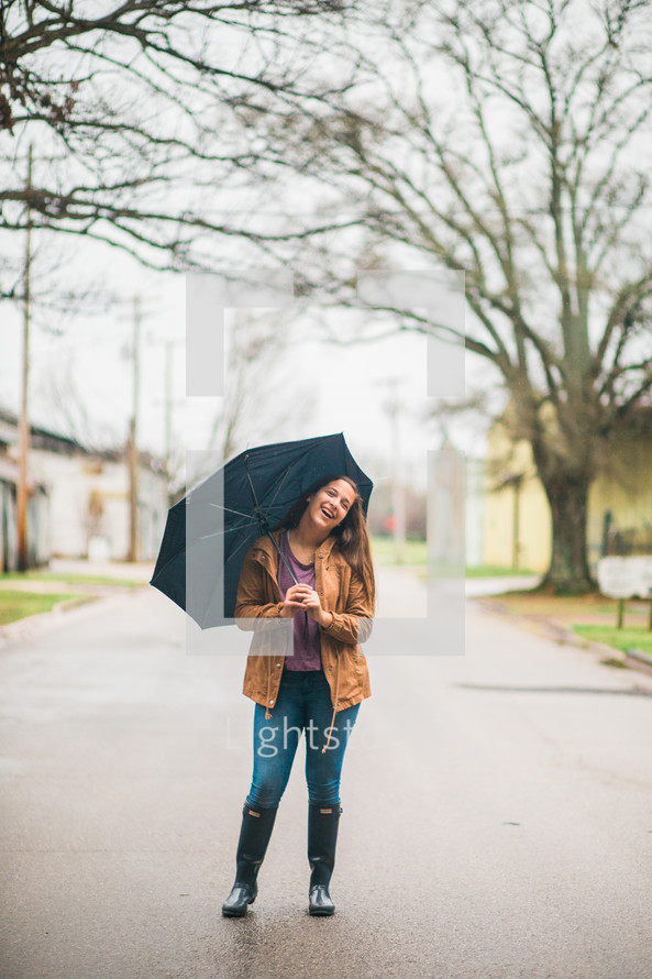 a teen girl holding an umbrella standing in the middle of a road 