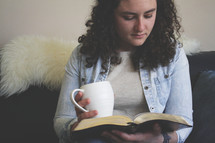a woman holding a mug reading a Bible 