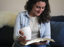 a woman holding a mug reading a Bible 