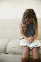 girl child with praying hands over the pages of a Bible 