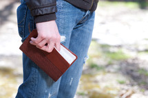 Man in jeans holding a Bible while standing outdoors.
