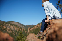 a woman sitting on a rock with view of mountains 