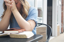 a woman sitting at an outdoor table praying with a coffee cup, Bible, and journal 
