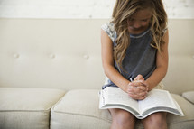 a girl child praying over an open Bible 