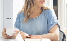 a woman sitting at an outdoor table with a coffee cup, Bible, and journal 