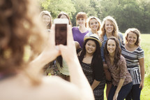 Group of young teenage women, posing for a picture being taken with a cell phone