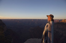 a woman wrapped in a blanket at the top of a canyon at sunset 