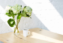 hydrangeas in a vase and coffee cup on a table 