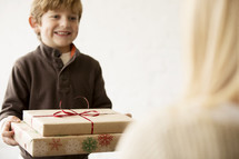 a young boy handing a Christmas gift to his mother 