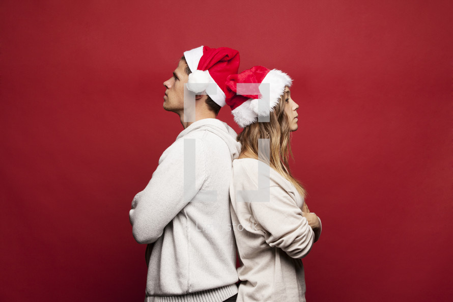 man and woman in santa hats back to back not speaking to each other