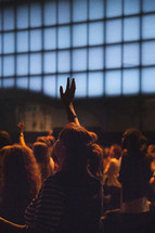 a woman standing with a raised hand at a worship service 