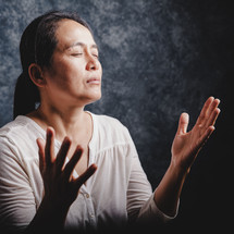 Asian woman praying with raised hands.