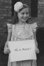 A little girl holding a He is Risen sign for Easter 