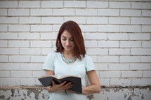 a young woman standing in front of a white wall and reading a Bible 