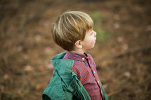 a toddler boy standing outdoors in a jacket 