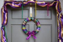 Festive Fat Tuesday garland and wreath in traditional Mardi Gras Purple, Gold, and, Green stripes on a front door 