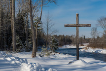 cross near a river and snowy landscape 