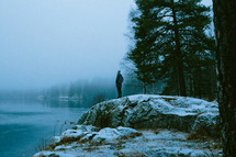 man standing on a rock by a lake shore in winter 