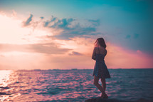 woman standing beside the ocean at sunset 