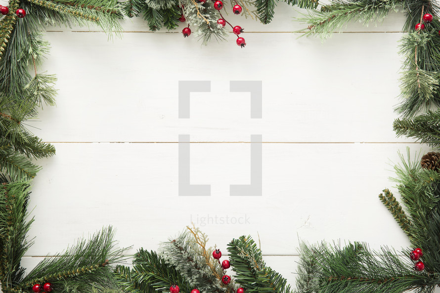 pine garland and berry border on white wood background.