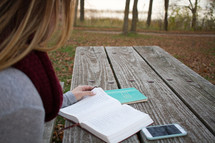 a woman sitting at a picnic table reading a Bible 