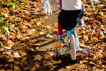 A little girl riding a bike with training wheels  in the autumn