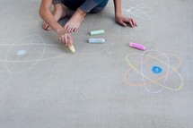 girl drawing an atom in sidewalk chalk 