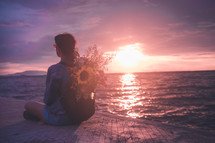 woman sitting with flowers in her backpack on a beach at sunset 