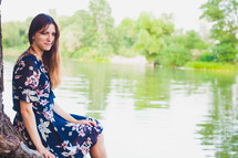 a woman in a floral dress sitting by a pond 