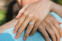 Hands with an engagement ring hugging a man's neck.