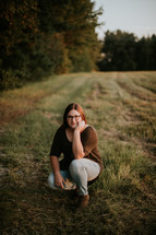 a woman squatting in a field at sunset 