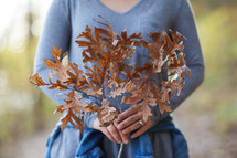 a woman holding a branch of brown fall leaves 