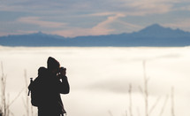 Silhouette of a man looking through binoculars at the sea and mountains.