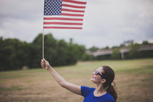 woman wearing stars and stripes sunglasses and a temporary tattoo - holding an American flag