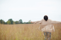 a woman with open arms walking through a field 