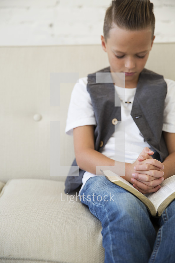 a boy child with praying hands over the pages of a Bible 