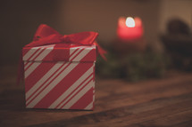 A red and white gift box and a candle on wood