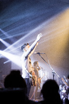 Guitar player with arms raised during concert performance on stage.